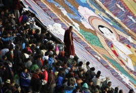 A Tibetan Buddhist monk stands between tourists and a giant thangka, a religious silk embroidery or painting unique to Tibet, during the Shoton Festival at Drepung Monastery on the outskirts of Lhasa, Tibet Autonomous Region, August 29, 2011.