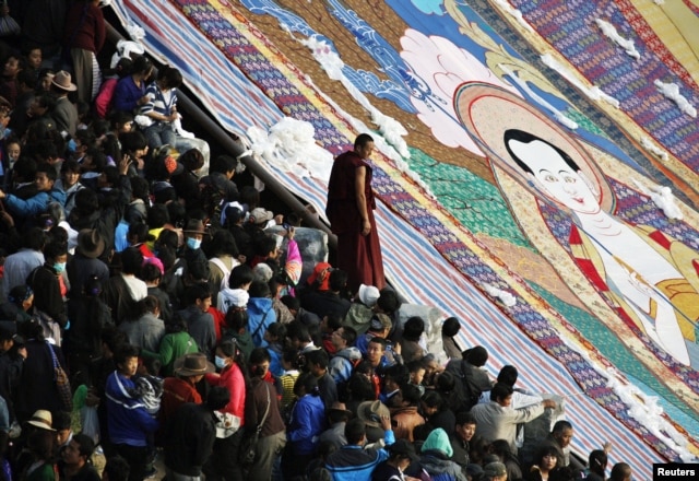 A Tibetan Buddhist monk stands between tourists and a giant thangka, a religious silk embroidery or painting unique to Tibet, during the Shoton Festival at Drepung Monastery on the outskirts of Lhasa, Tibet Autonomous Region, August 29, 2011.