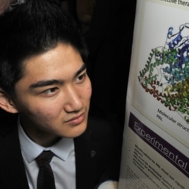 Jack Li poses with his poster board, which explains his research on a therapy for a rare genetic disease.