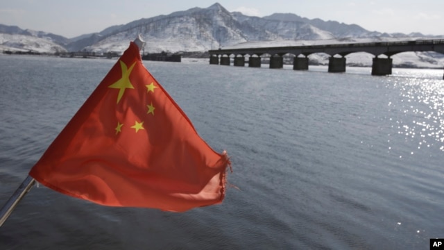 A Chinese flag is hoisted near the Hekou Bridge, right, linking China and North Korea, which was bombed in the 1950's during the Korean War, in Hekou, China, February 7, 2013.