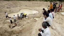 Local villagers sit and observe others preparing for a memorial service at a grave site of Phnom Trungbat in Do Dontrei village, about 60 kilometers (40 miles) northwest of Siem Reap in Cambodia, Thursday, Aug. 9, 2012. More than 100 people attended a Buddhist ceremony in rural Cambodia at the site of a freshly dug Khmer Rouge mass grave. Buddhist monks led prayers and people came with offerings of food and drinks Thursday, five days after about 20 skulls and bone fragments were unearthed at the site of a former Khmer Rouge prison. (AP Photo/Heng Sinith)