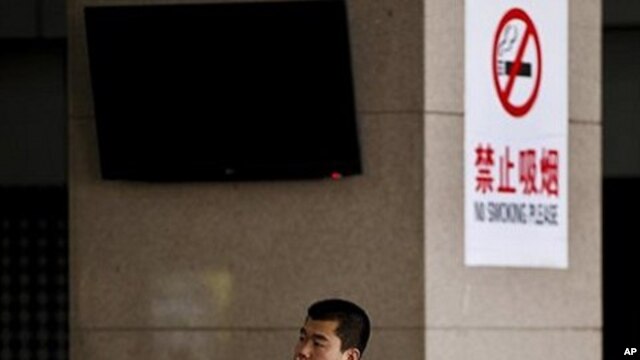 A Chinese man smokes in front of a pillar with a no smoking notice on display at a bus station in Beijing, March 24, 2011