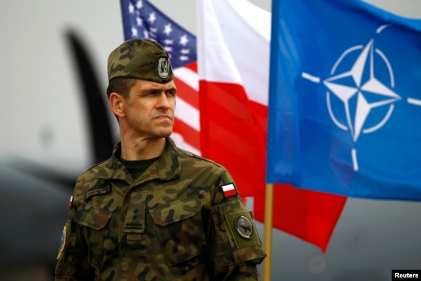 FILE - A Polish soldier stands in front of U.S., Polish and NATO flags ahead of military exercises in Swidwin, northwestern Poland, April 23, 2014.