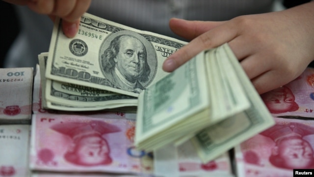 Seorang pegawai bank menghitung lembaran dolar Amerika di atas tumpukan yuan China. (Foto: Ilustrasi)