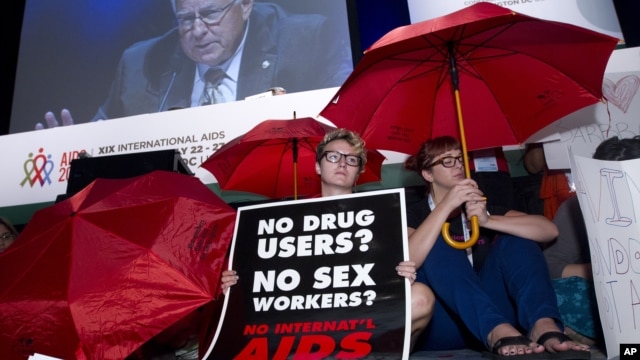 People protest in front of the stage as Sen. Mike Enzi is seen on a giant video screen during the XIX International AIDS Conference in Washington, July 25, 2012.
