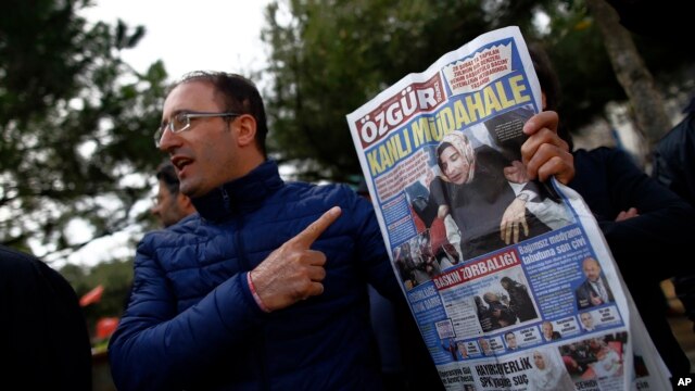 FILE - A man shows the front page of the daily Ozgur with a headline that reads " bloody intervention" as people gather outside the headquarters of Zaman newspaper in Istanbul, March 6, 2016. 