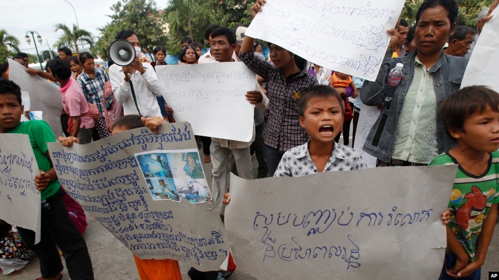 FILE - A boy holds a banner reading "Please stop grabbing our land" at a rally by evection victims in front of the National Assembly in Phnom Penh, Cambodia, Sept. 1, 2014.