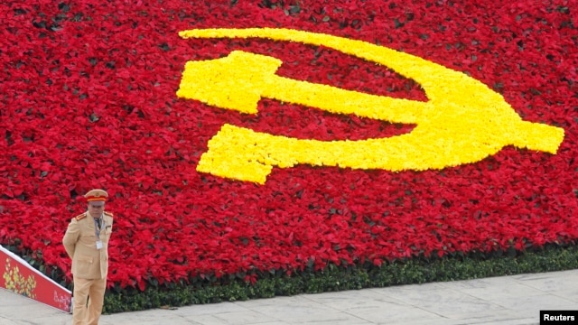 Một cảnh sát đứng bảo vệ bên cạnh logo đảng cộng sản được trang trí bằng hoa tại Trung tâm Hội nghị Quốc gia, Hà Nội.
