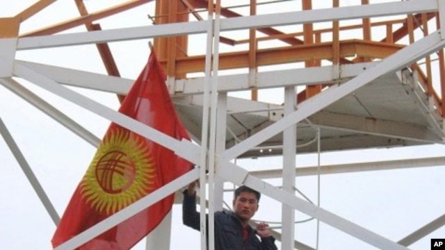 Flag-waving demonstrator climbing a tower at the Kyrgyz Defense Ministry, in  Bishkek, 14 Apr 2010