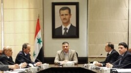 In this undated photo released by the Syrian official news agency on Aug. 5, 2012, Syrian Prime Minister Riad Hijab, center, speaks under the portrait of the Syrian President Bashar Assad during a meeting in Damascus, Syria.
