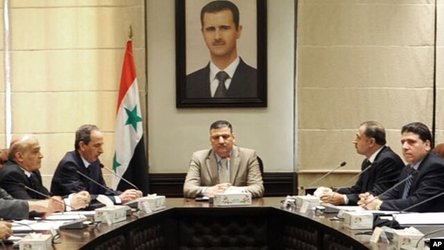 In this undated photo released by the Syrian official news agency SANA on Sunday, Aug. 5, 2012, Syrian Prime Minister Riad Hijab, center, speaks under the portrait of the Syrian President Bashar Assad during a meeting in Damascus, Syria.
