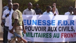 A soldier walks past Malians protesting the junta's arrest of several prominent figures in April