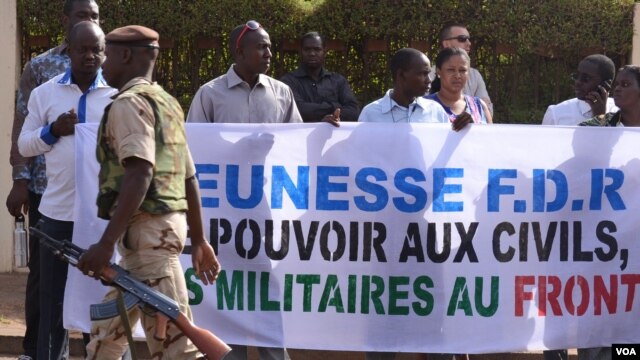 A soldier walks past Malians protesting the junta's arrest of several prominent figures in April