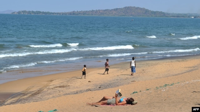 A woman reads a book as young boys pass by on the Saga beach at Lake Malawi, July 17, 2011.  