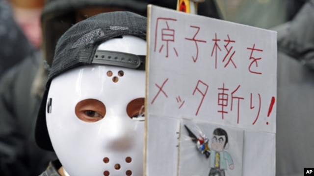 A protester wearing a mask holds a sign at a rally, in front of the headquarters of Tokyo Electric Power Company [TEPCO], aimed at criticizing TEPCO and demanding the abolition of nuclear power, in Tokyo,  March 3, 2012. 