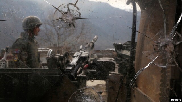 An Afghan National Army (ANA) soldier is seen through damaged glass as he keeps watch at the Forward Base in Nari district near the army outpost in Kunar province, Feb. 24, 2014