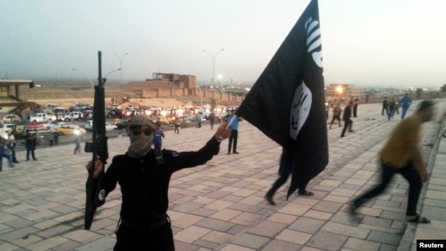 Seorang pejuang Negara Islam (ISIS) memegang bendera ISIS dan senjata di Mosul, Irak.