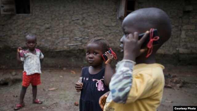 Olematu, 3, center, and Ibrahim, 4, talk on toy phones in a village near Kenema, Sierra Leone. Their 15-year-old sister, Betty, has taken charge after their mother’s death from Ebola. Betty survived an Ebola infection. (© UNICEF / Bindra) 