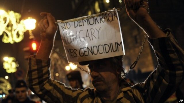 A Hungarian protester dressed as a prisoner holds a banner during a demonstration against Prime Minister Viktor Orban and against the country's new constitution in Budapest, Hungary, Monday, Jan. 2, 2012.