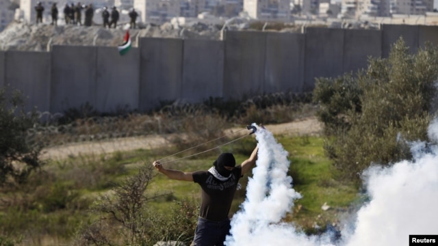 A Palestinian stone-throwing protester uses a sling to throw back a tear gas canister fired by Israeli security officers (rear) during clashes in the West Bank village of Bilin near Ramallah, January 4, 2013. 