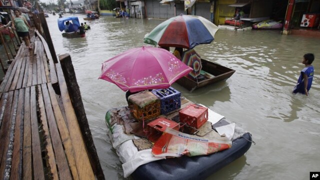 Residents use makeshift floats as others cross a makeshift bridge built over a flooded road in suburban Pasig, east of Manila, Philippines, August 15, 2012.