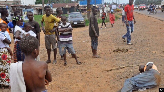 People stand around a man, right, suspected of suffering from the Ebola virus in a main street and busy part in Monrovia, Liberia, Friday, Sept. 12, 2014.