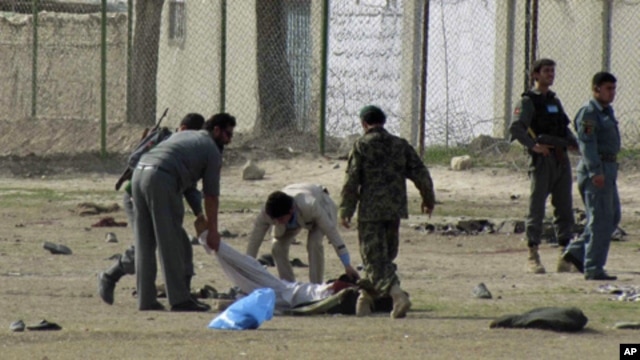 Afghan policemen and security personnel pick up a dead body after a suicide attack at an army recruitment center in Kunduz, March 14, 2011.