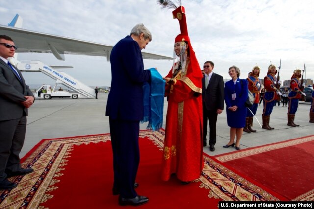 U.S. Secretary of State John Kerry accepts a gift of aaruul -- dried cheese curds -- from a woman in traditional Mongolian dress greets as he arrives at Chinggis Khaan International Airport in Ulaanbataar, Mongolia, June 5, 2016.