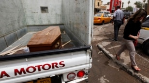 A woman walks past a truck carrying a wooden coffin of a man killed during an attack on liquor stores in Baghdad, Iraq, May 15, 2013. 