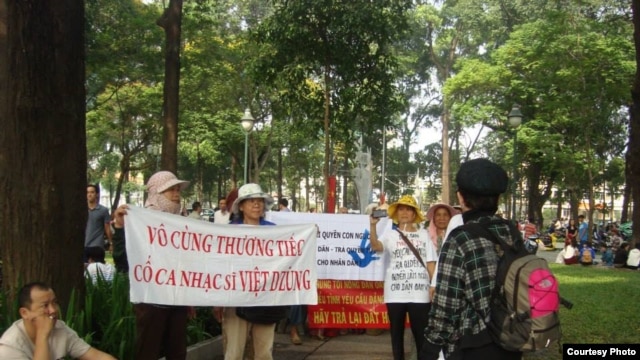 Người biểu tình mang băng rôn với hàng chữ ‘Vô cùng thương tiếc cố nhạc sĩ Việt Dzũng’.