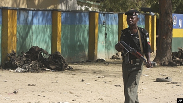 A police officer walks past an engine block of a suicide bomber's vehicle by the wall of the state police headquarters in Kano, Nigeria, January 24, 2012.
