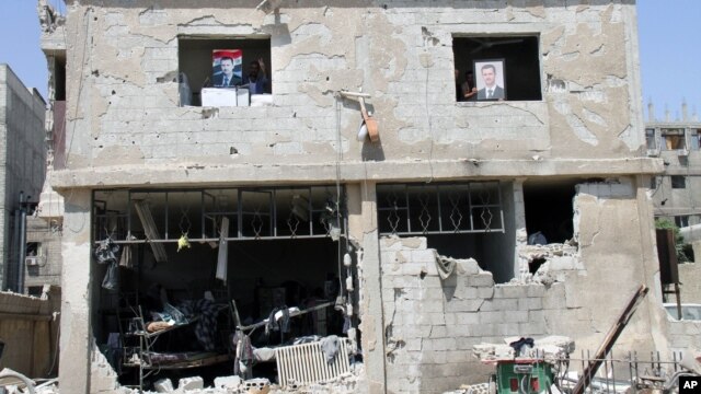Syrian security forces officers hold portraits of Syrian President Bashar Assad from the windows of their building, which was destroyed after a car bomb exploded near the shrine of Sayyida Zeinab, in a suburb of Damascus, Syria, June 14, 2012.