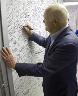 John Glenn signs the wall of the clean room leading into space shuttle Discovery in Orbiter Processing Facility-1 OPF-1 at NASA's Kennedy Space Center in Florida. Glenn is at the space center to mark the 50th anniversary of being the first American astron