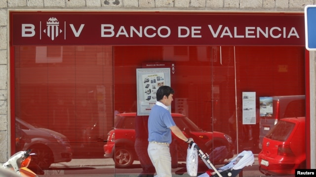 A man pushes a pram past a Banco de Valencia bank branch in Madrid, June 25, 2012. 