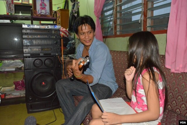 Ông bố Rodrigo Wage chơi một khúc nhạc cho đứa con gái 8 tuổi sau một ngày dài làm việc nhà. (Ảnh: Simone Orendain/VOA)