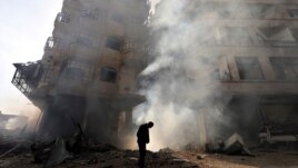 A man walks in front of a burning building after a Syrian Air force air strike in the Ain Tarma neighborhood of Damascus January 27, 2013. 