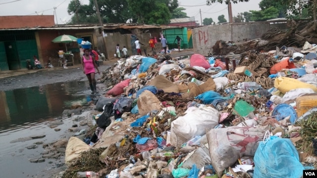 Angola, Luanda. Uma mulher atravessa o amontoado de lixo de galochas calçadas