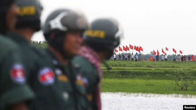 Cảnh sát Campuchia đứng canh gác trong lúc người Việt phất cờ từ bên kia biên giới giữa hai nước.