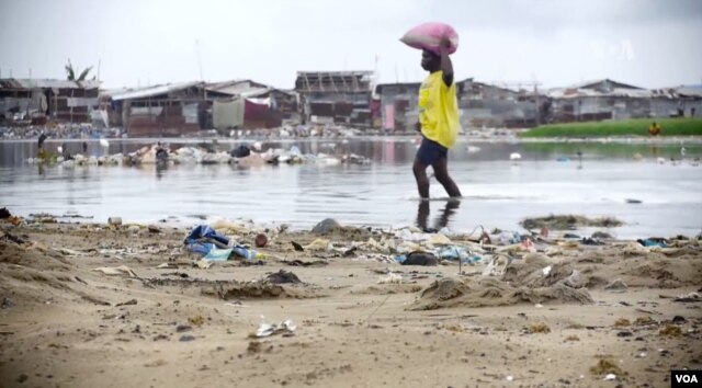 A woman wades near a beach in Monrovia, Liberia. Though poverty does not discriminate, women have fewer resources to cope. (B. Muchler/VOA News)