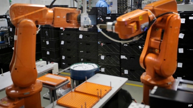 File - A Chinese worker is seen behind orange robot arms at work at Rapoo Technology factory in southern Chinese industrial boomtown of Shenzhen, Aug. 21, 2015.
