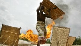 An unidentified woman carries her tapioca after drying it near a gas flare belonging to the Shell oil company in Utorogun, Nigeria, March 5, 2006 (file photo).