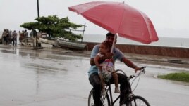A man balances a child and umbrella on his bike as it rains during the approach of Hurricane Sandy in Manzanillo, Cuba, Oct. 24, 2012.
