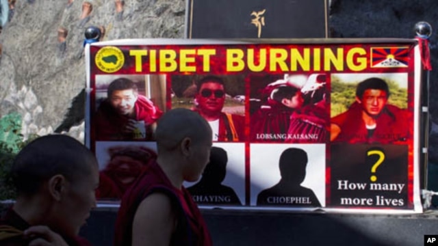 Tibetan Buddhist nuns pass by a poster showing pictures of those who have self-immolated since March, Dharmsala, India, Oct. 19, 2011.