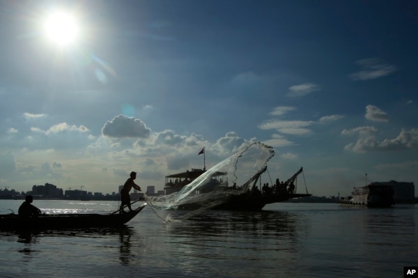 FILE - A fisherman casts his fishing net next to a ferry in the Mekong river near Phnom Penh, Cambodia, Tuesday, Dec. 1, 2015.