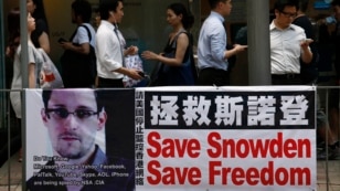 People carrying mobile phones walk past a banner supporting Edward Snowden, a former contractor at the National Security Agency (NSA), at Hong Kong's financial Central district, June 18, 2013. 