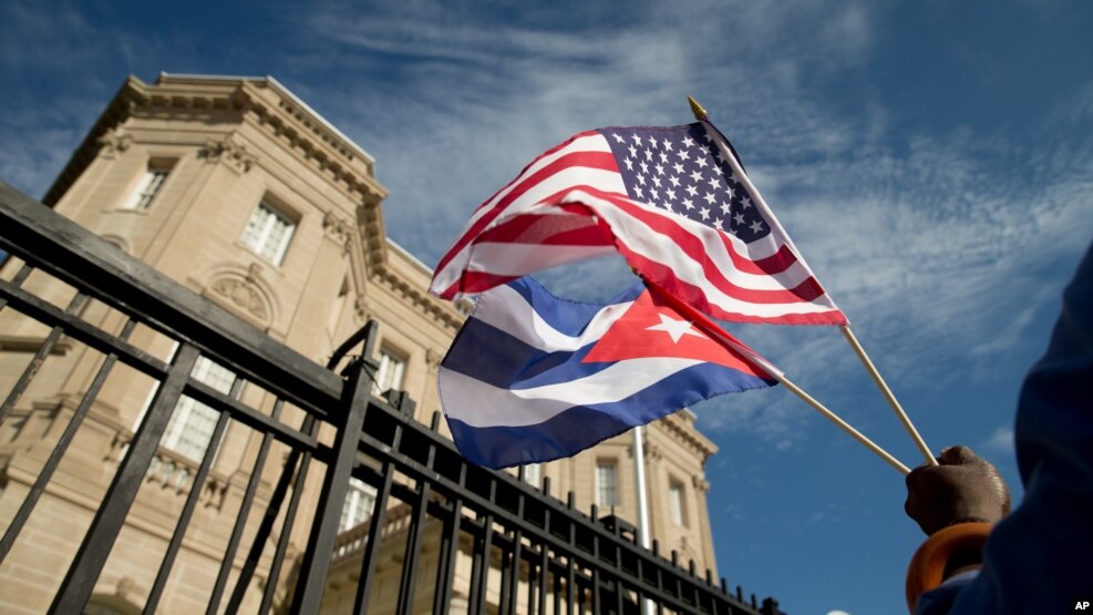 Edwardo Clark, một người Mỹ gốc Cuba, cầm quốc kỳ Mỹ và quốc kỳ Cuba đứng bên ngoài đại sứ quán mới mở của Cuba tại Washington, 20/7/2015.