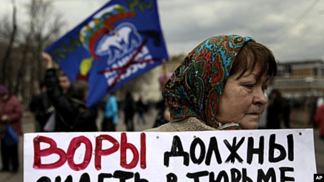 A member of the opposition holds a banner at a protest near the Kremlin, April 16, 2011. The banner reads, "Thieves should go to jail" and displays images of Prime Minister Vladimir Putin.