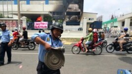 Một nhà máy bị đốt và biểu ngữ căng trước cửa với hàng chữ 'Chúng tôi yêu Việt Nam. Hãy bảo vệ chén cơm'.