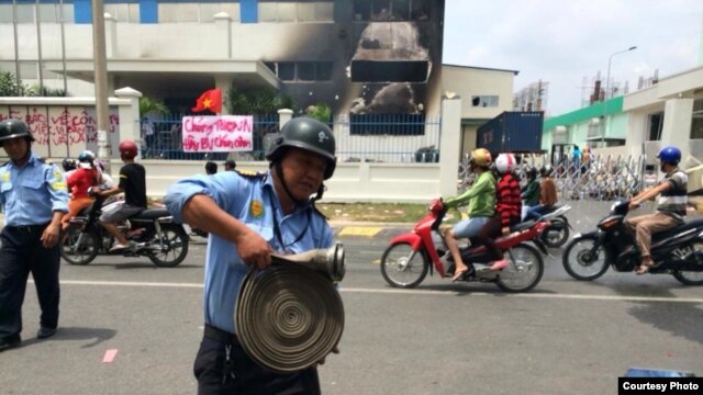 Một nhà máy ở Bình Dương bị đốt. Phía trước là biểu ngữ với hàng chữ 'Chúng tôi yêu Việt Nam. Hãy bảo vệ chén cơm."