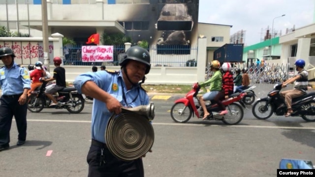 Một nhà máy ở Bình Dương bị đốt. Phía trước là biểu ngữ với hàng chữ 'Chúng tôi yêu Việt Nam. Hãy bảo vệ chén cơm."